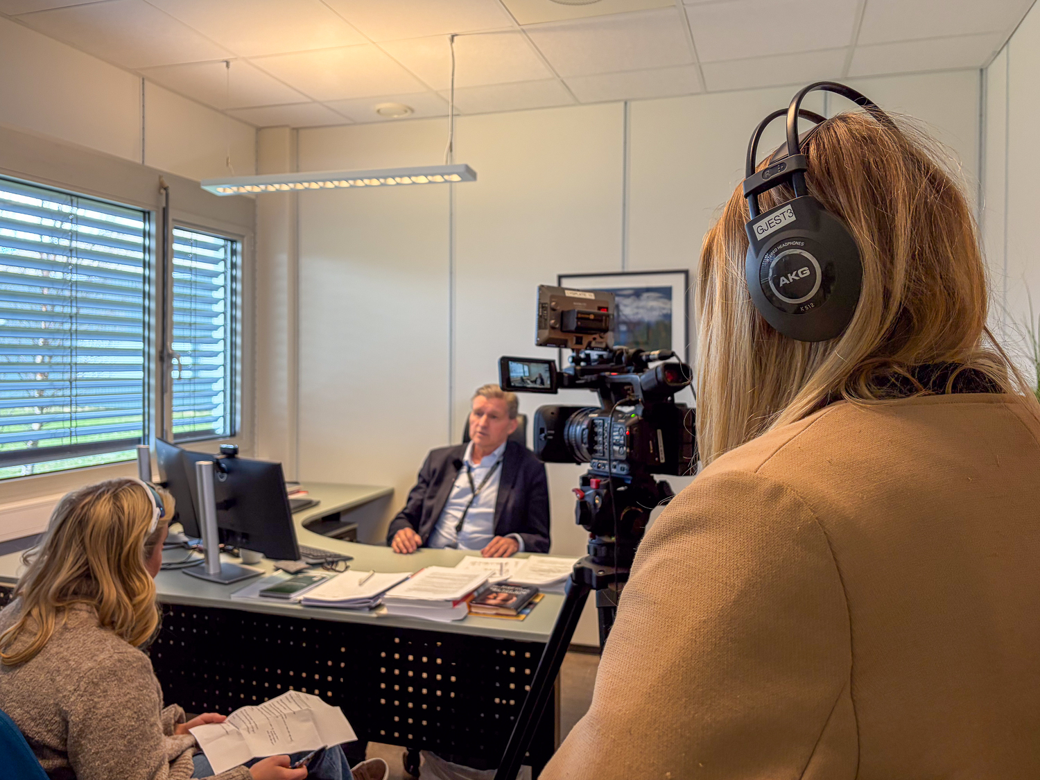 En mann sitter ved en pult, han blir intervjuet av to kvinner.