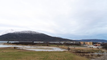 Bilde av Fjelldal med fjære i forgrunnen, brann- og redningsskolens bygg i midten og fjell i bakgrunnen.