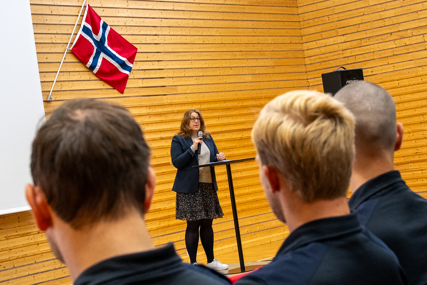 Dame står foran publikum og snakker. Det norske flagget på hennes venstre side