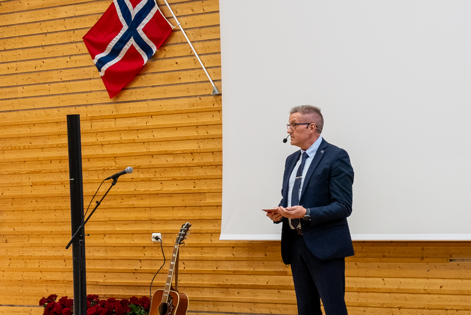 Mann i dress står foran et publikum og taler. 