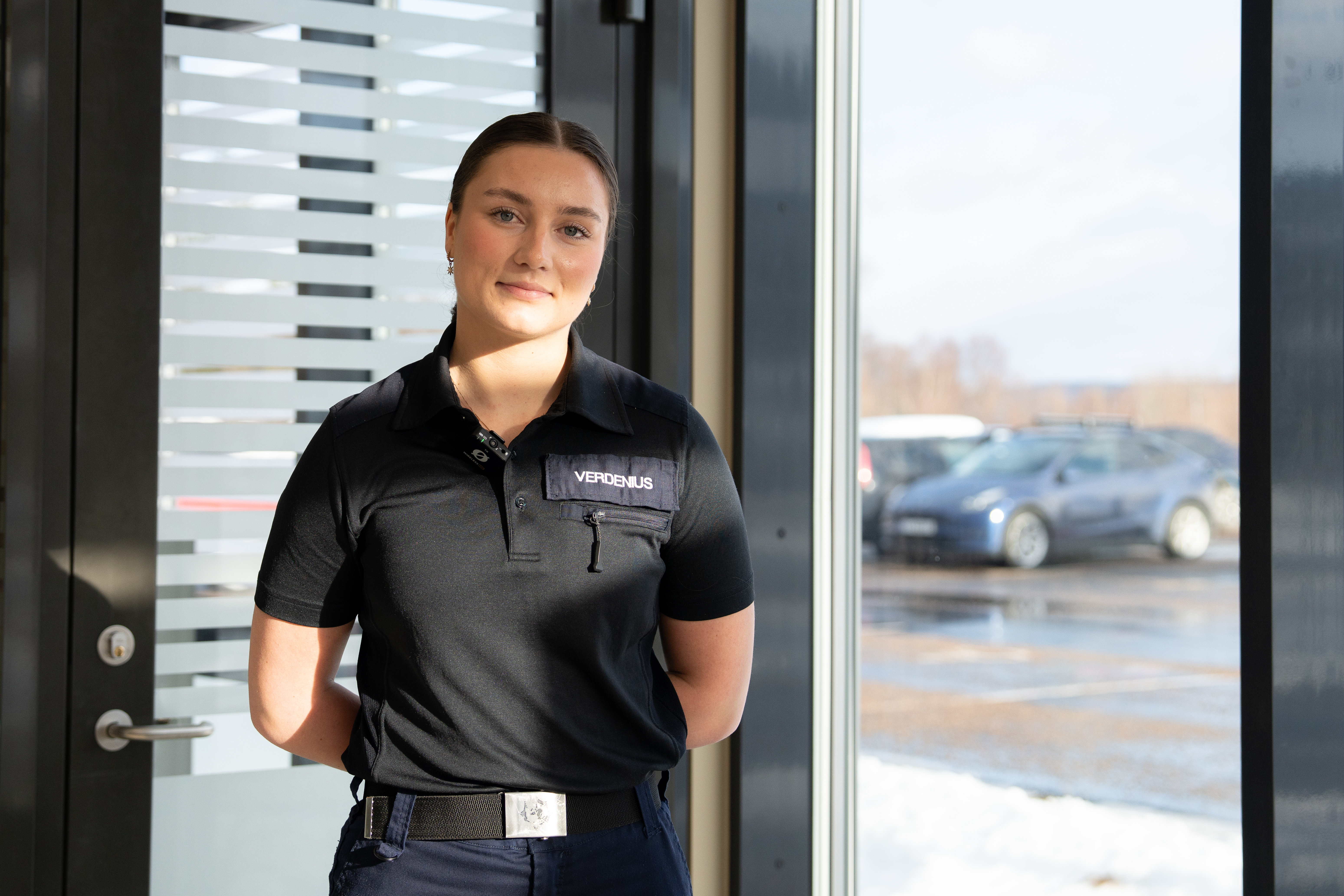 Kvinnelig student i uniform står foran et vindu og en glassdør