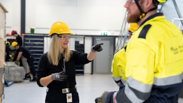 Kvinnelig lærer med gul hjelm gir instrukser til mannlige studenter. Foto