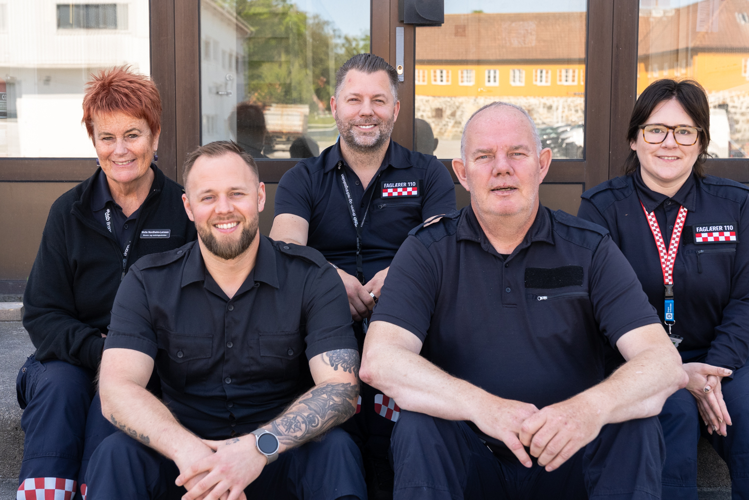 Fem mennesker sitter uniformert på en trapp og smiler mot kamera. Tre menn og to kvinner