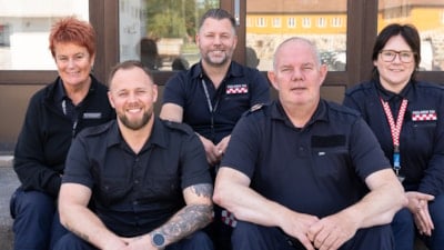 Fem mennesker sitter uniformert på en trapp og smiler mot kamera. Tre menn og to kvinner