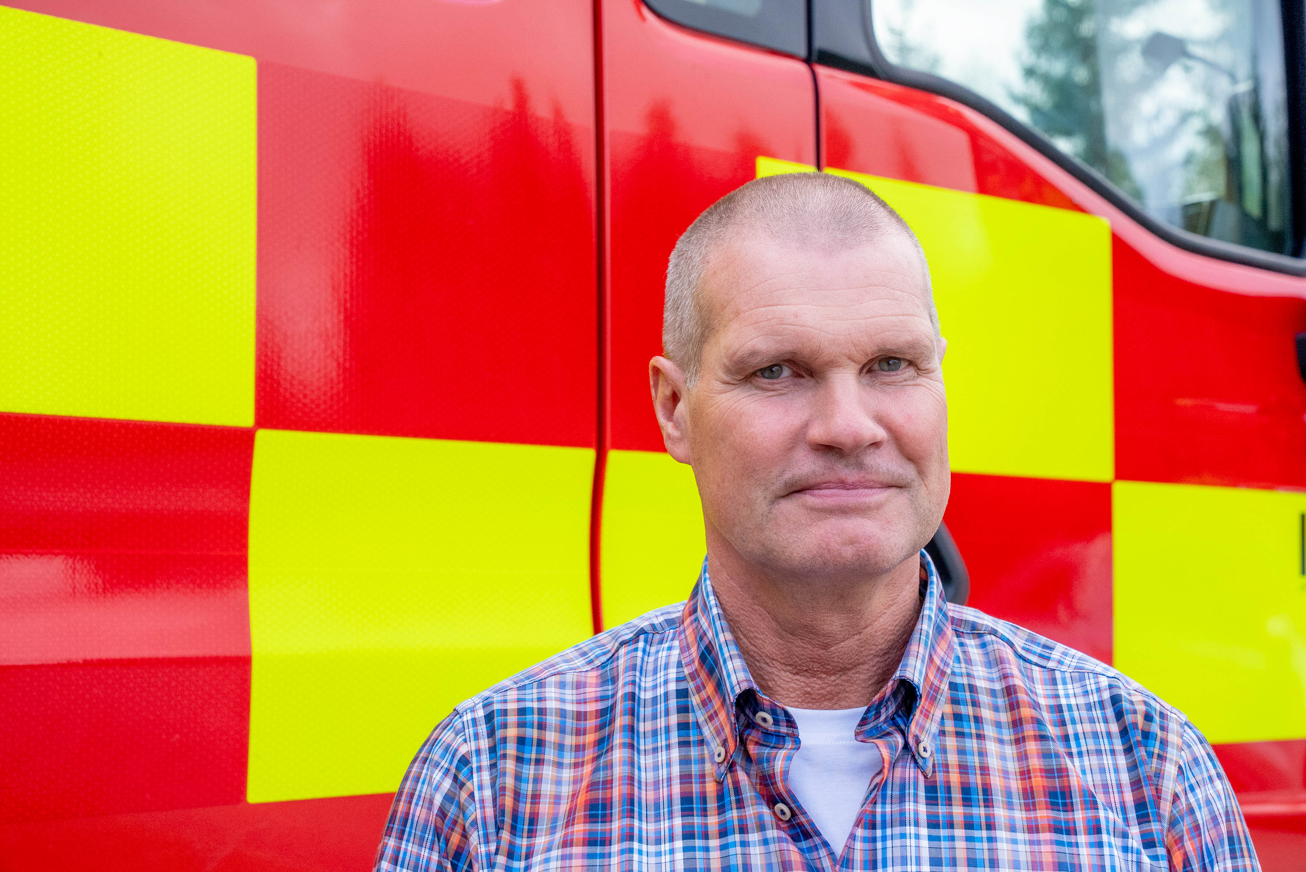 Mann ser rett inn i kamera. I bakgrunnen er en rød og gul brannbil. Foto
