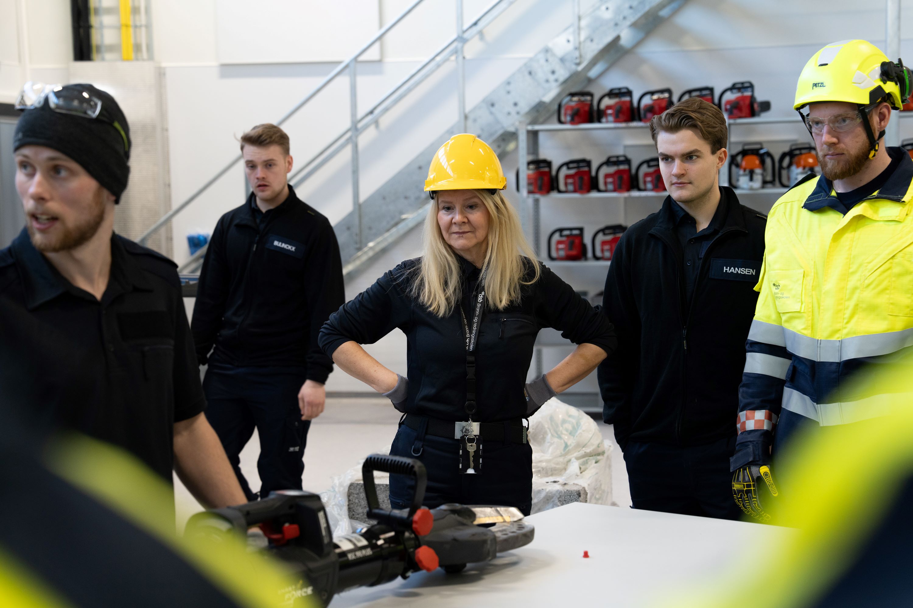 Dame med sikkerhetshjelm står midt mellom flere menn. Foto