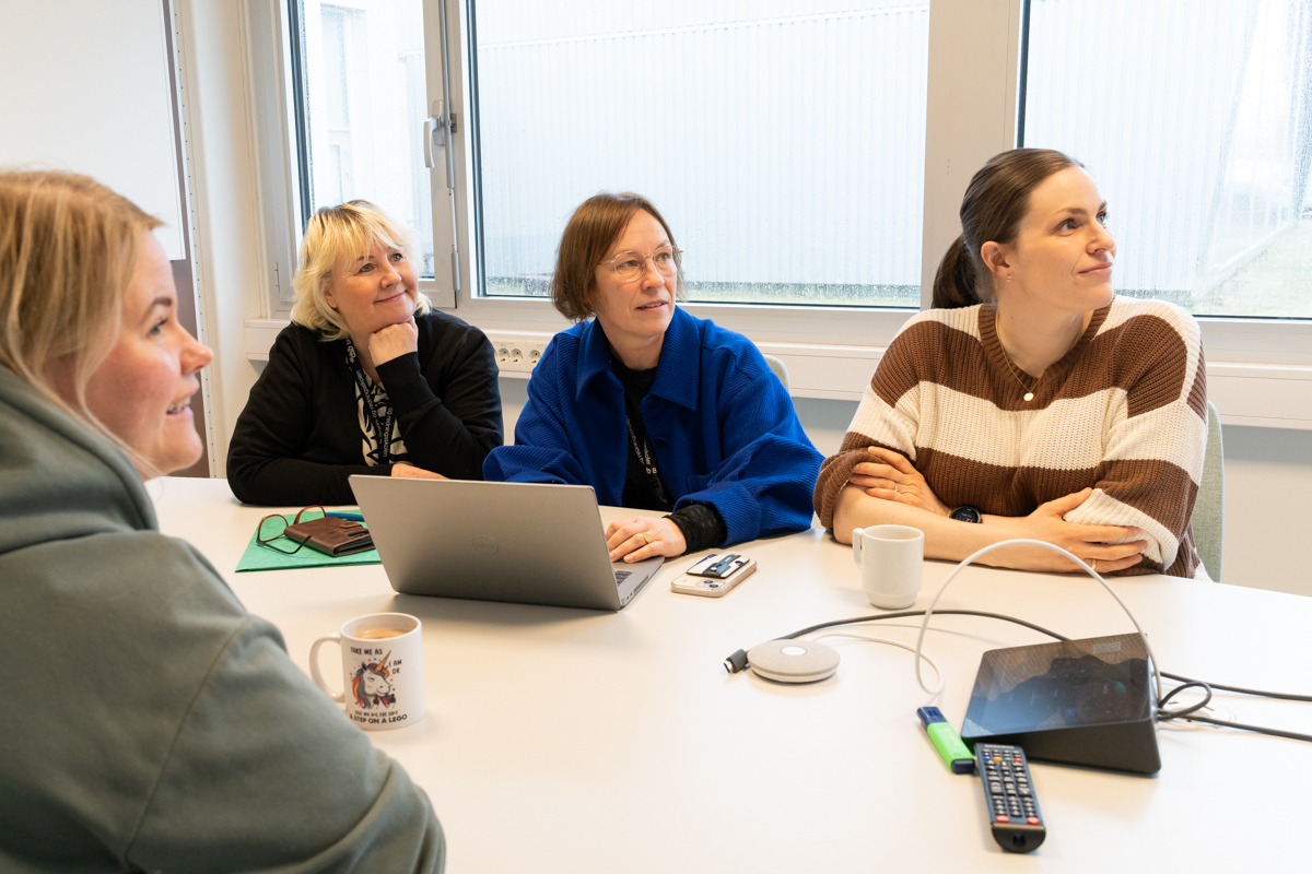 Fire kvinner som sitter rundt et bord. Alle ser mot venstre.