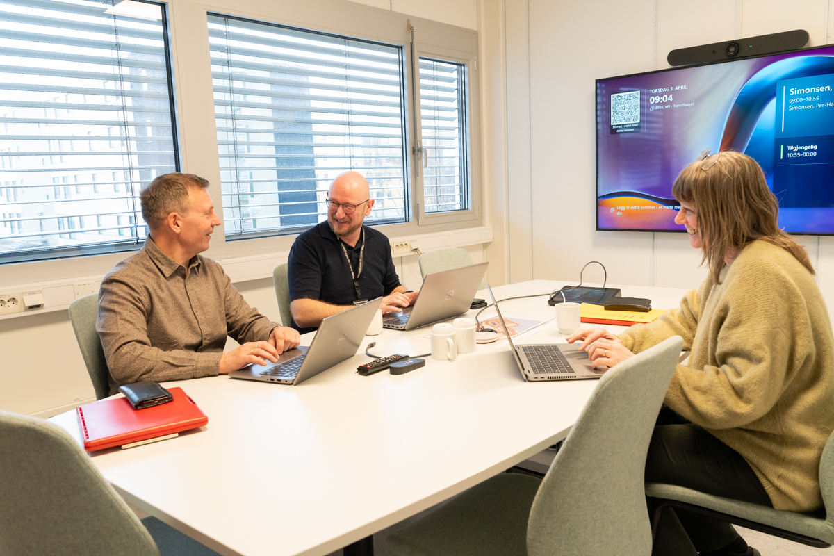 To menn og en kvinne rundt et møtebord. Foto