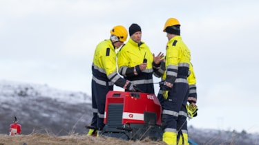 Fire mennesker i trafikkdress står på en høyde rundt en maskin. Foto