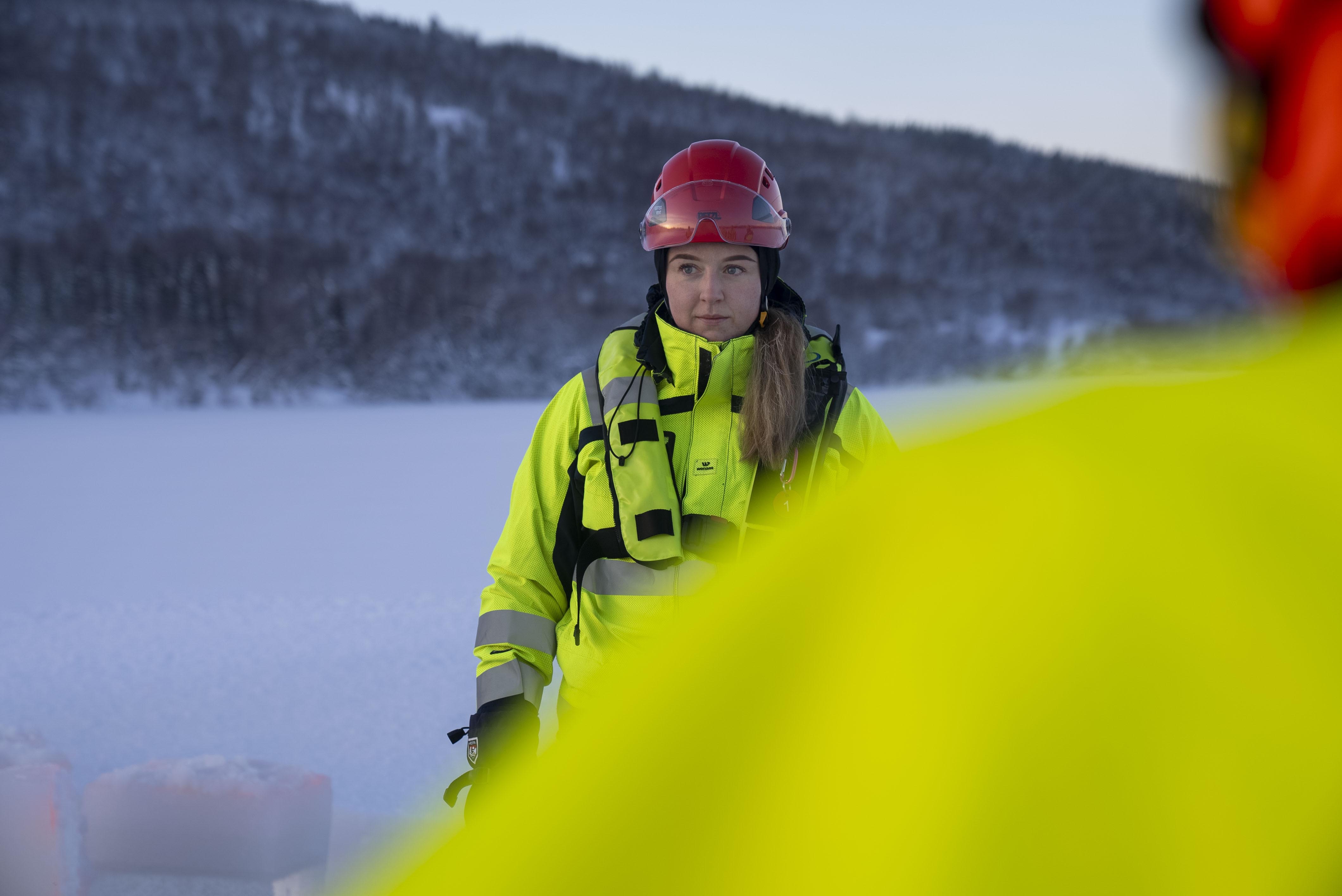 Kvinne i trafikkdress og rød hjelm, ute i arktiske omgivelser