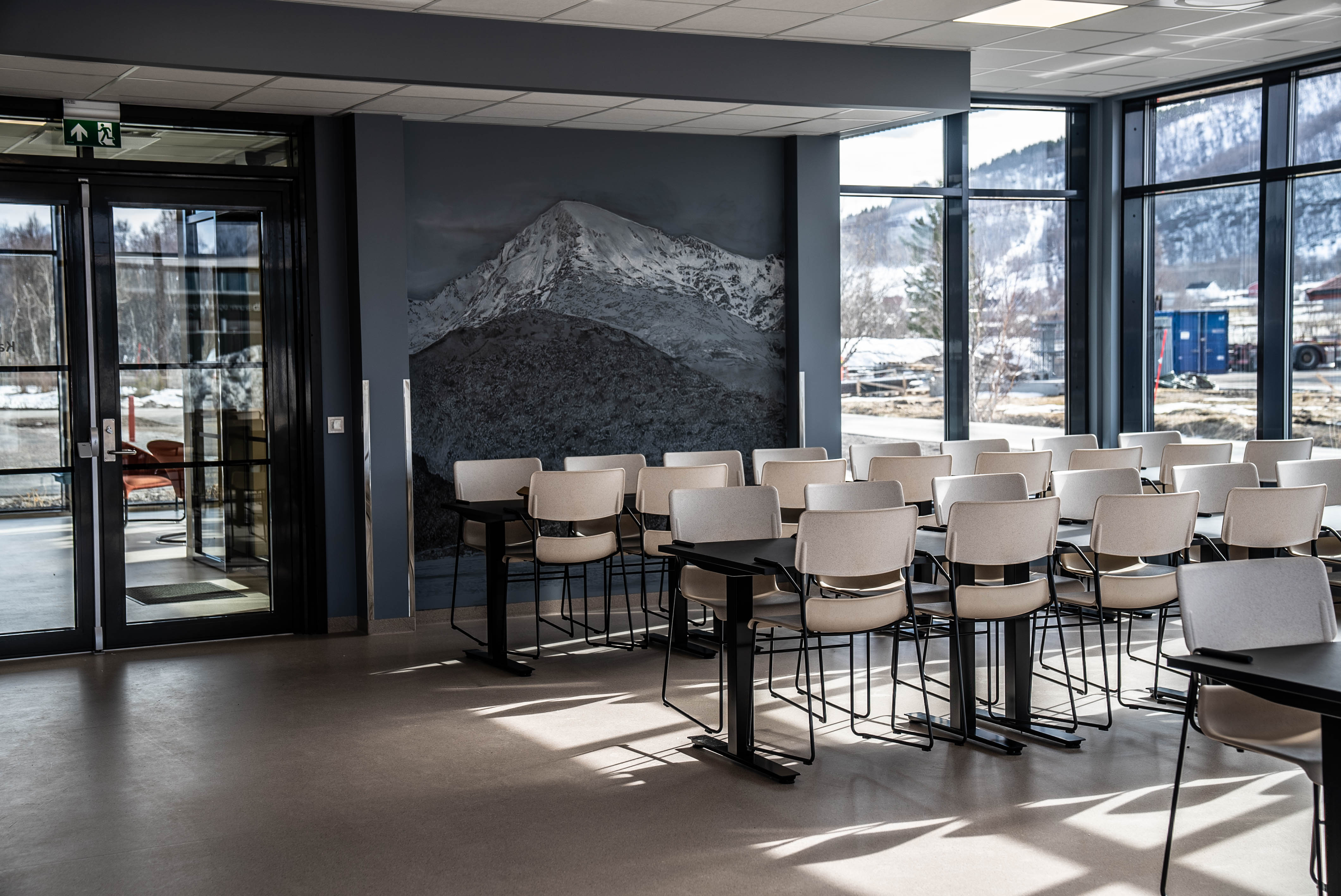 Et tomt bord og mange stoler. I bakgrunnen er et fjell malt på en vegg. Foto