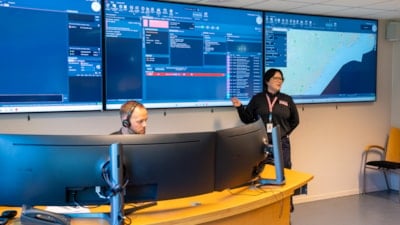 En mann sitter bak to skjermer. En dame står foran tre skjermer som viser kart og data