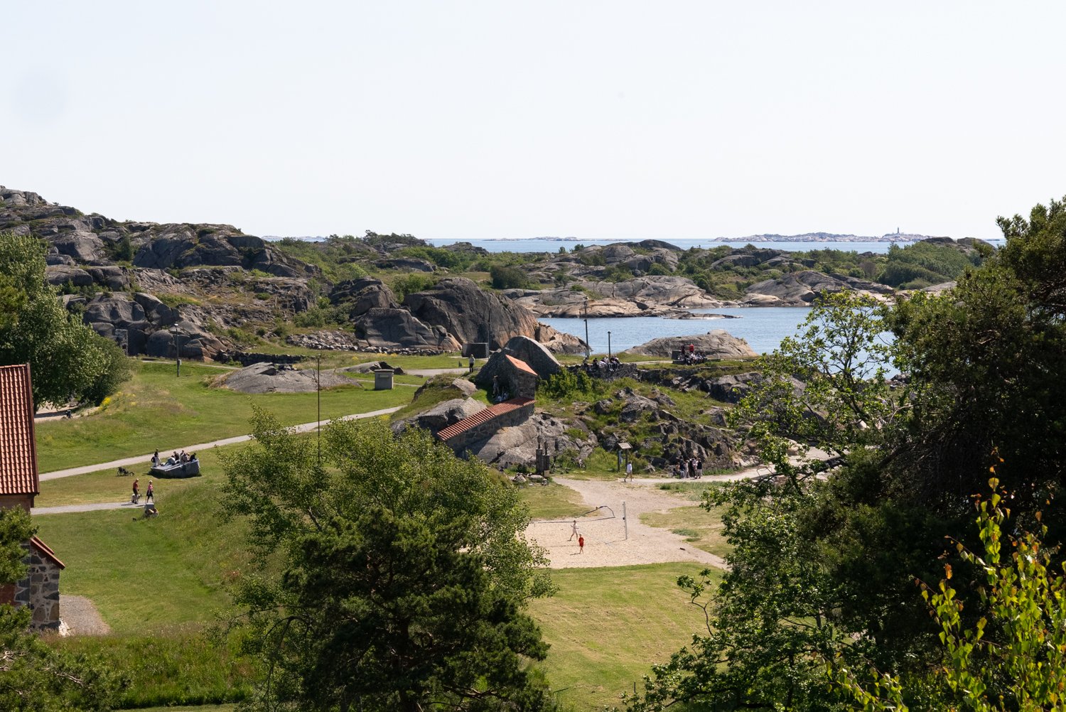 Utsikt over fjord, grønt gress, berg og en sandvolleyballbane