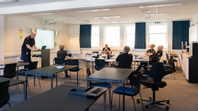 Et stort klasserom med noen få studenter og en lærer som står foran