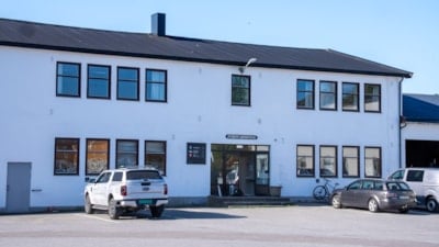 Et hvit mursteinsbygg med mange vinduer og tre biler parkert foran