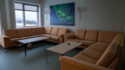 En stor oransje sofa med to bord og et bilde av nordlys i bakgrunnen.