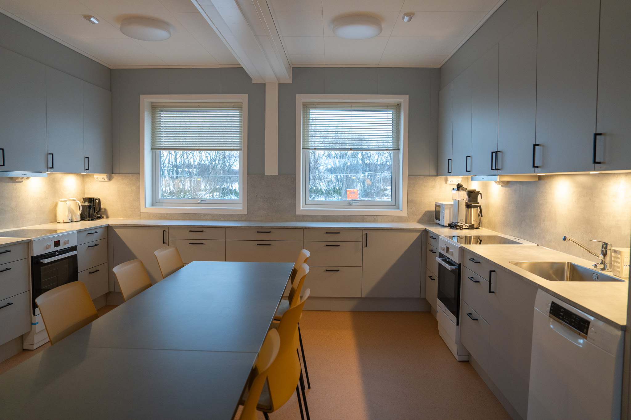 Et spisebord og en kjøkkeninnredning. To vinduer.