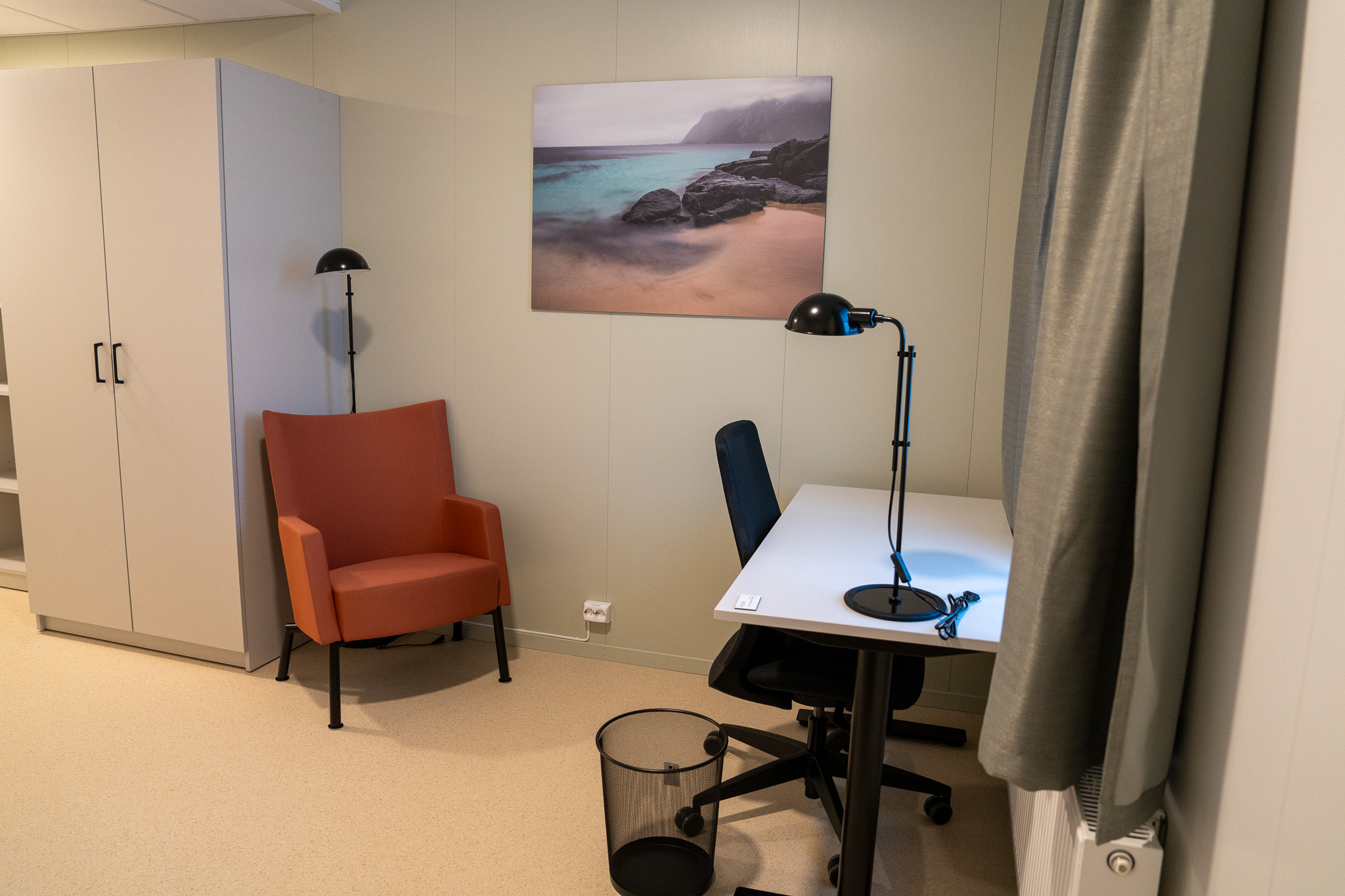 Et stort skap, en oransje godstol, et skrivebord og en kontorstol