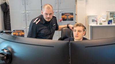 To mannlige operatører sitter bak skjermer på en 110-sentral
