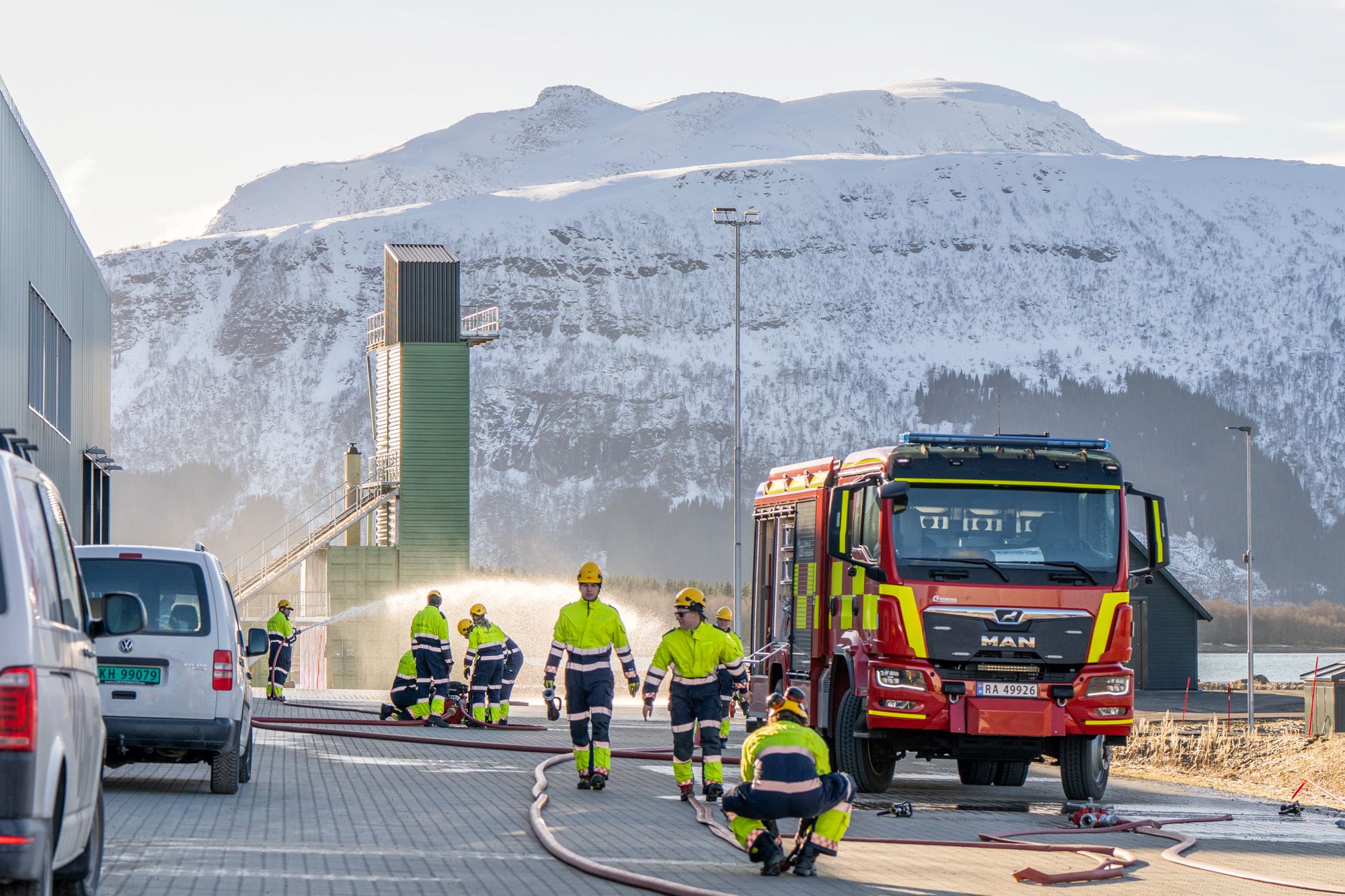 Studenter i trafikkdress utenfor brannstasjonen, ved siden av en brannbil. En høyderigg i bakgrunnen. Foto