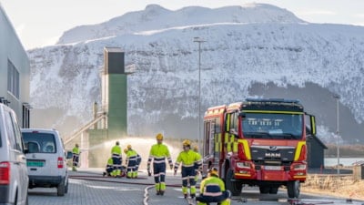 Studenter i trafikkdress utenfor brannstasjonen, ved siden av en brannbil. En høyderigg i bakgrunnen. Foto