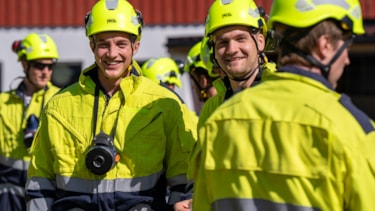 Brannkonstabelstudenter kledd i trafikkdresser smiler mot kamera