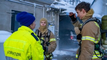 Instruktør står med ryggen til kamera og snakker med to studenter i røykdykkerbekledning. Foto
