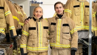 To studenter i brannbekledning holder armen rundt hverandre og smiler mot kamera