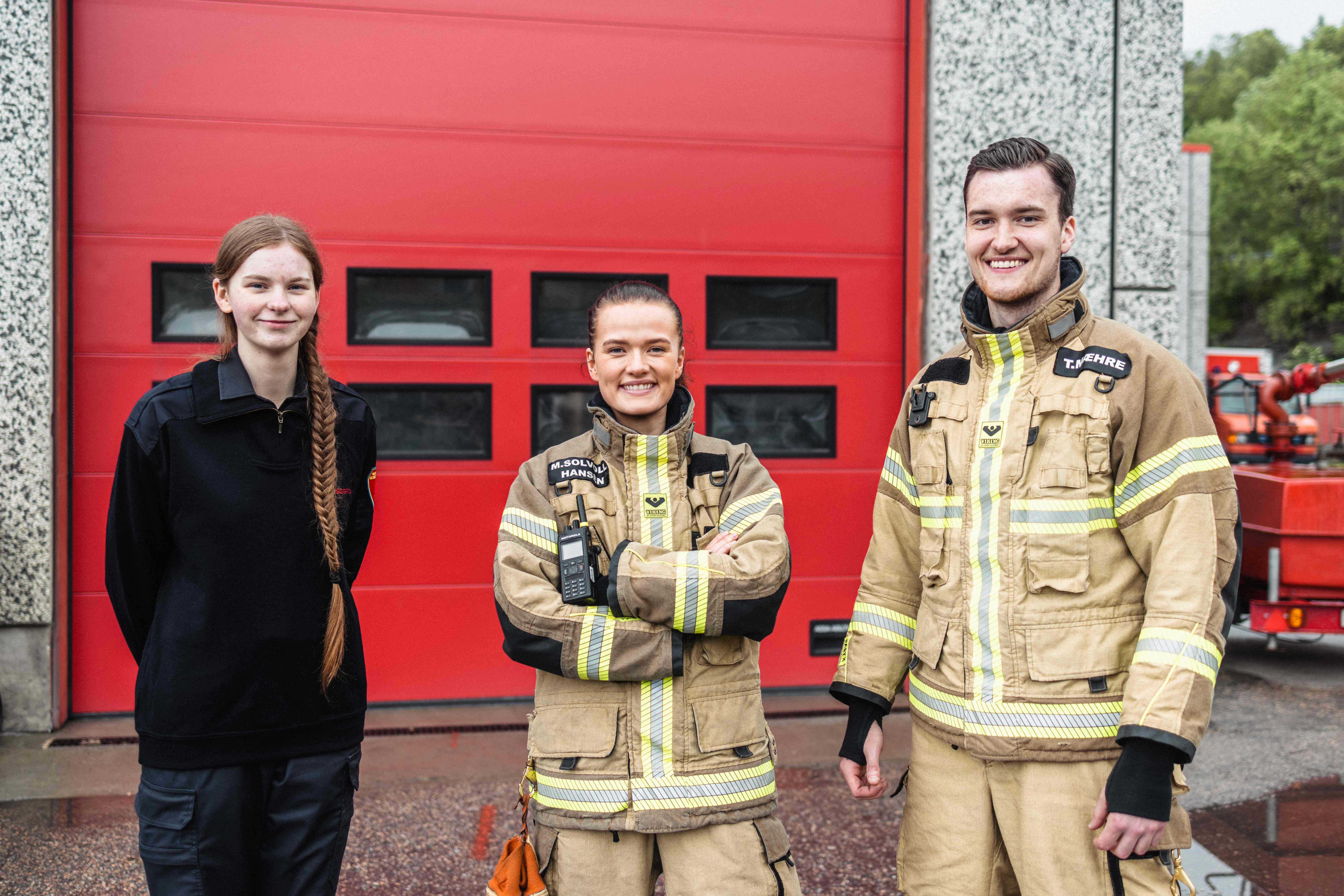 En kvinnelig brannforebygger, en kvinnelig brannkonstabel og en mannlig brannkonstabel ikledd uniform smiler mot kamera