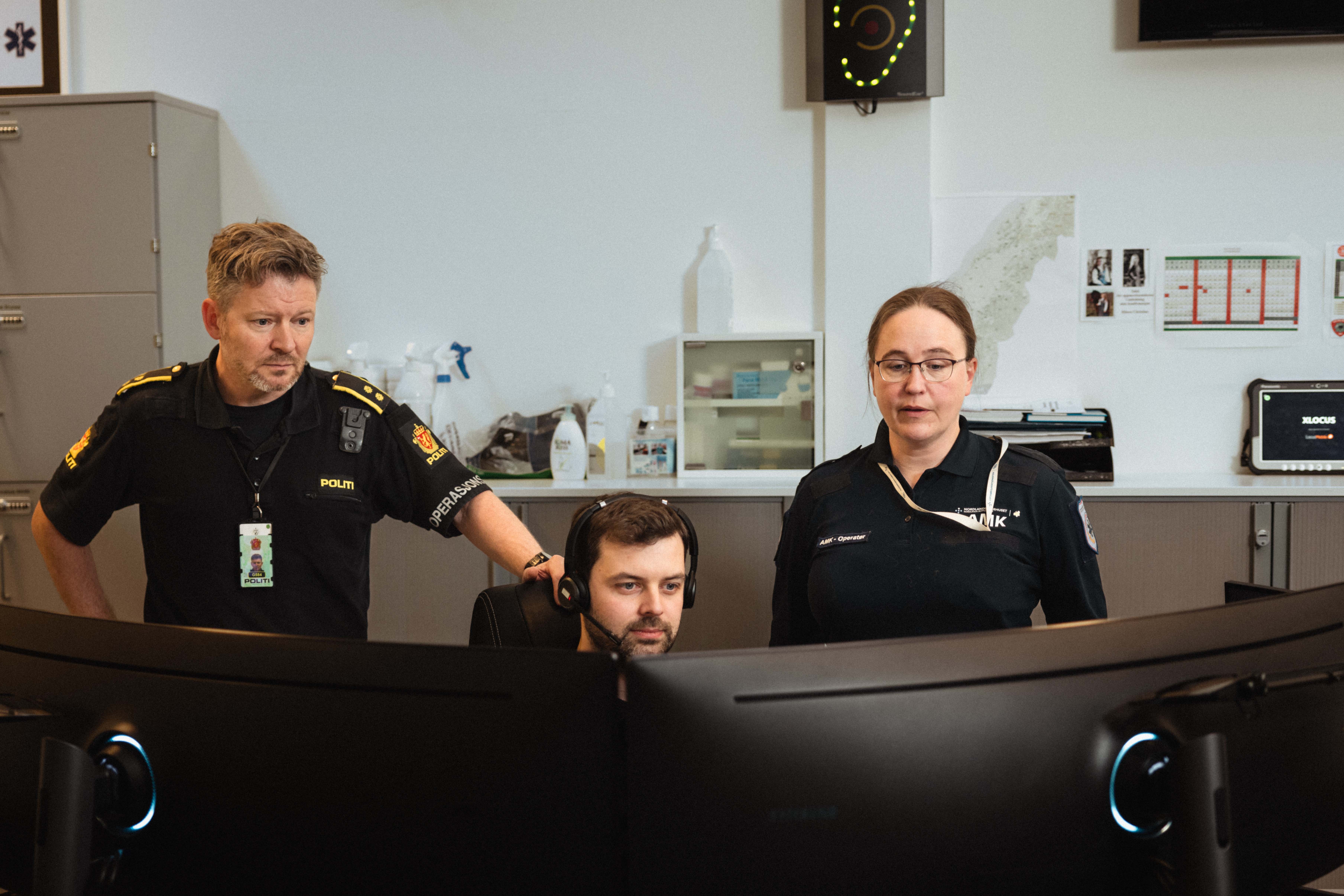En mann og en dame står bak en sittende alarmsentraloperatør