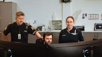 En mann og en dame står bak en sittende alarmsentraloperatør