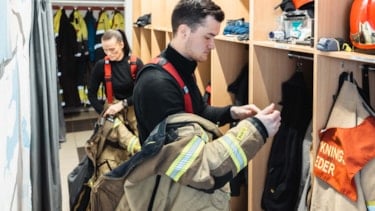 To brannkonstabler kler på seg røykdykkerdrakt i garderoben