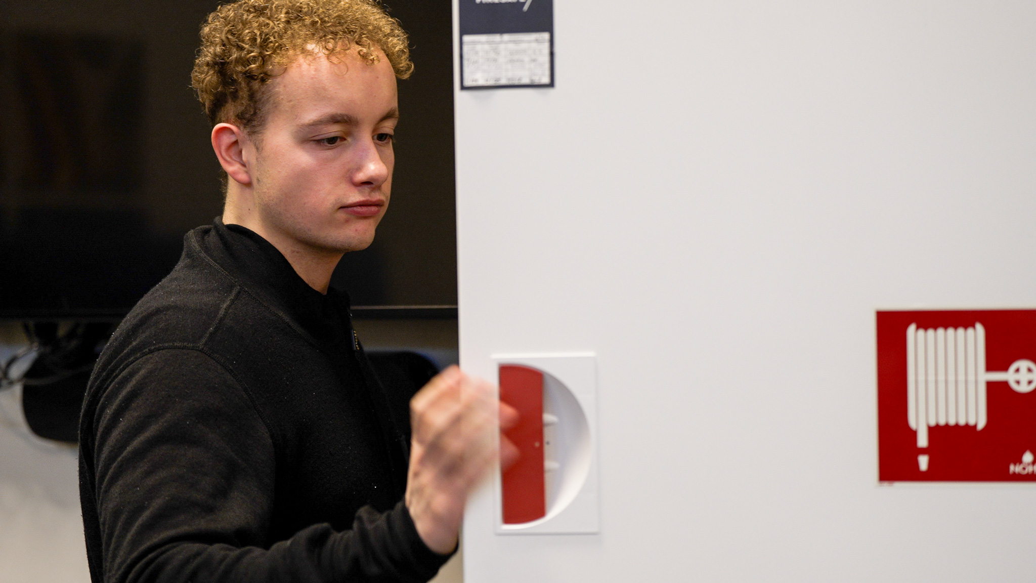 Mann holder i døra til et skap med brannslangetrommel i. Foto