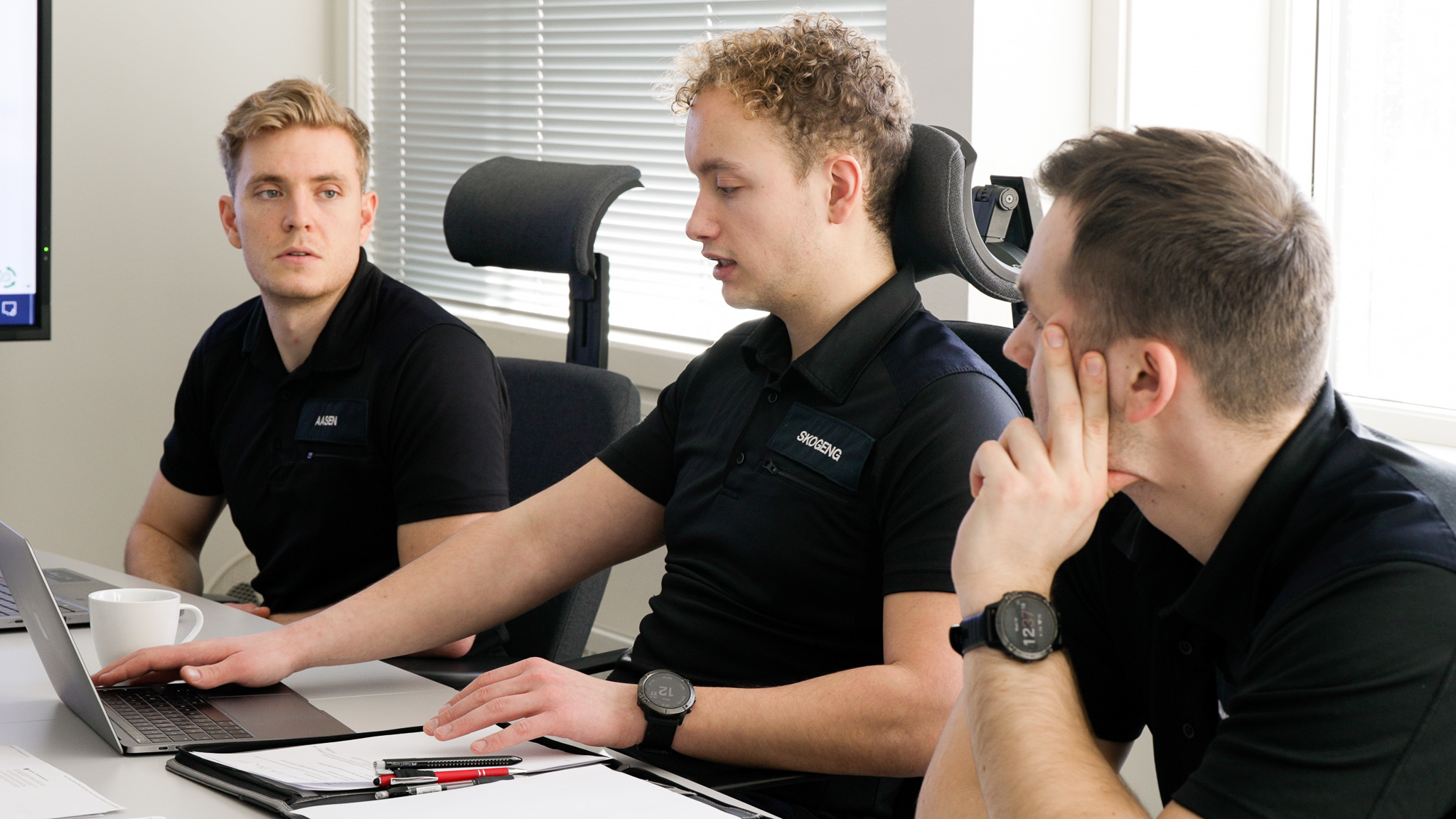 Tre mannlige studenter i uniform sitter ved et bord og diskuterer