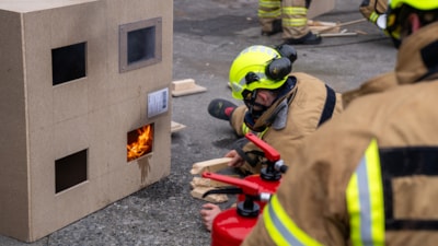 Studenter i brannbekledning tester brannfysikk i liten husmodell
