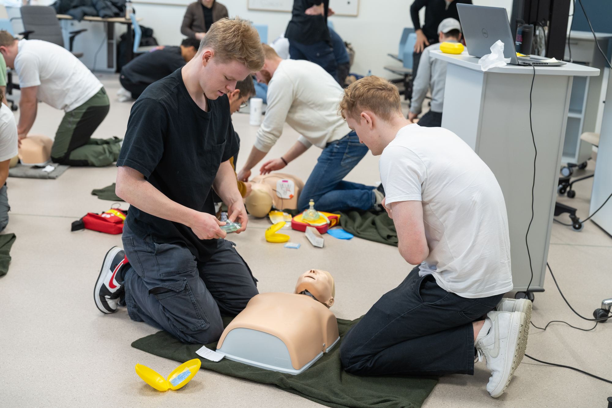 To mannlige studenter står ved en dukke og øver på livreddende hjelp. Foto