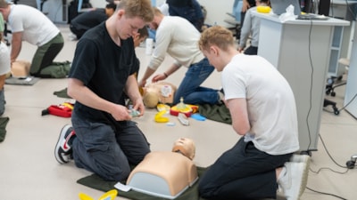 To mannlige studenter står ved en dukke og øver på livreddende hjelp. Foto