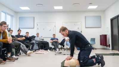 Lærer demonstrerer førstehjelp på dukke med studenter sittende rundt. Foto