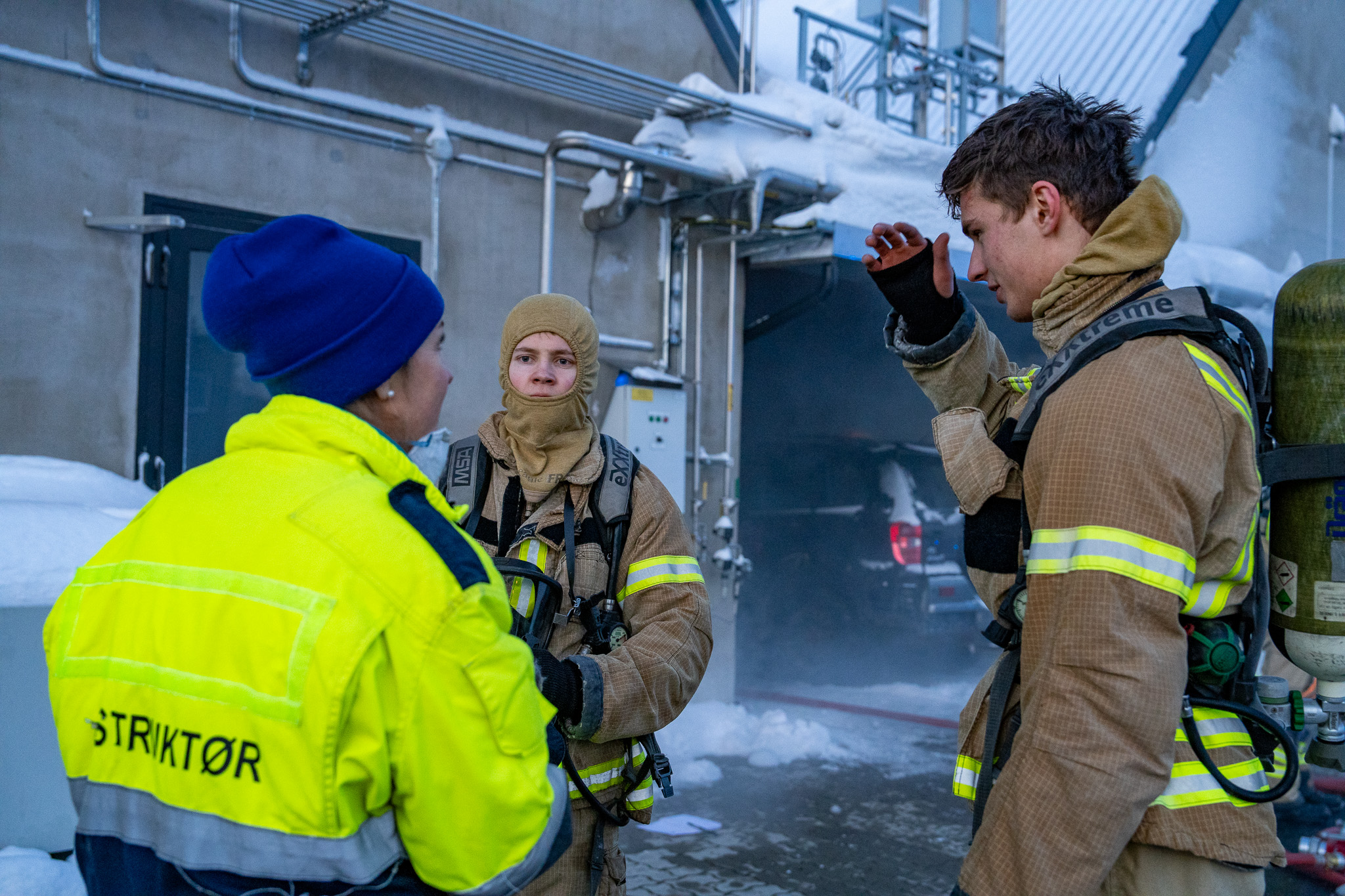 To mannlige studenter i brannbekledning i samtale med lærer