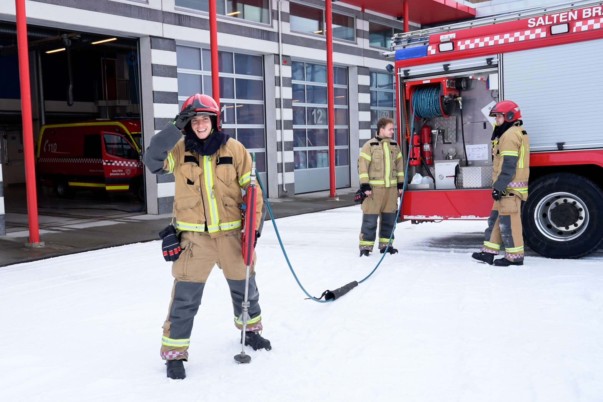 Brannkonstable står foran med skjærslokker i hånden. Bak ved brannbilen står to brannkonstabler.