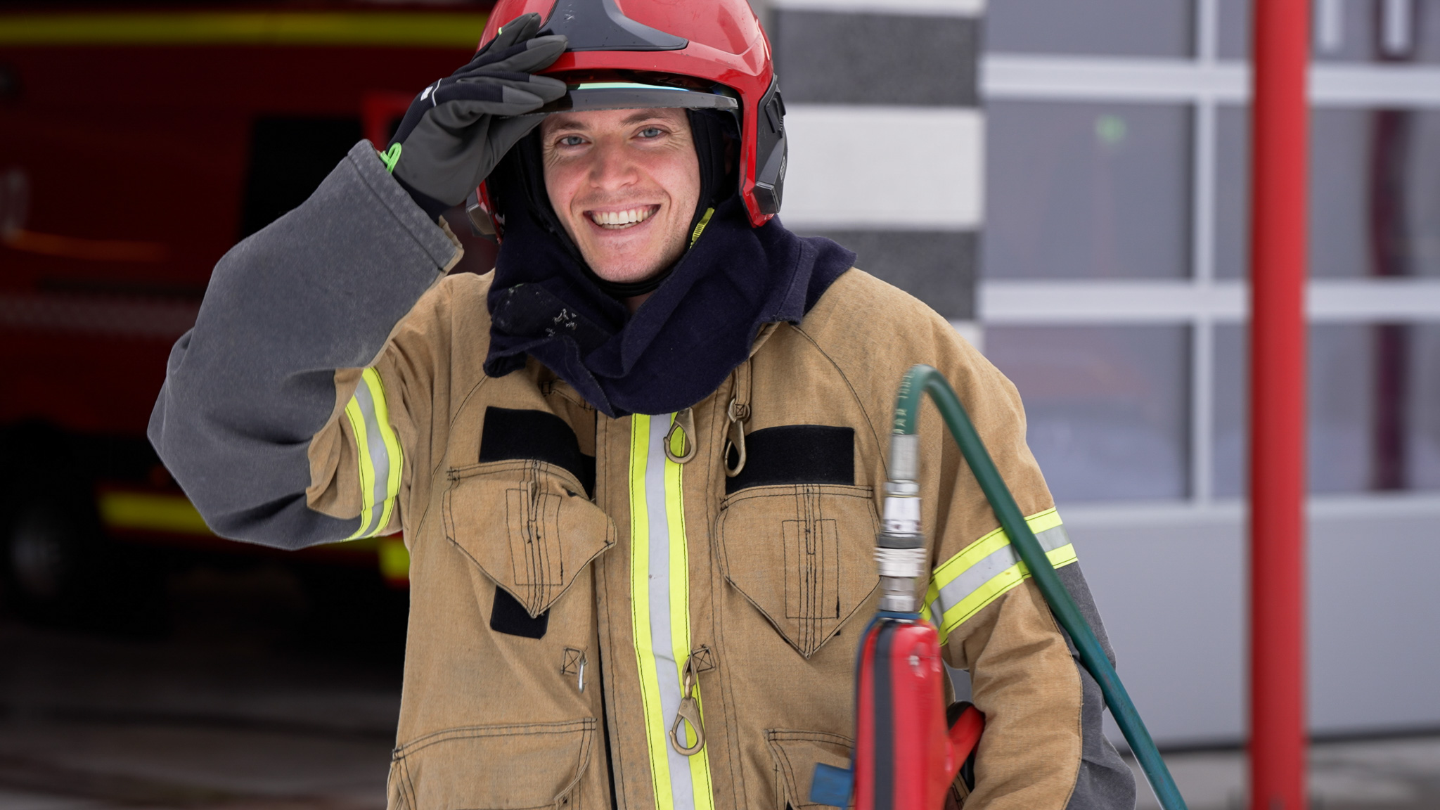 Nærbilde av smilende brannkonstabel med hjelm og skjørslokker i hånden