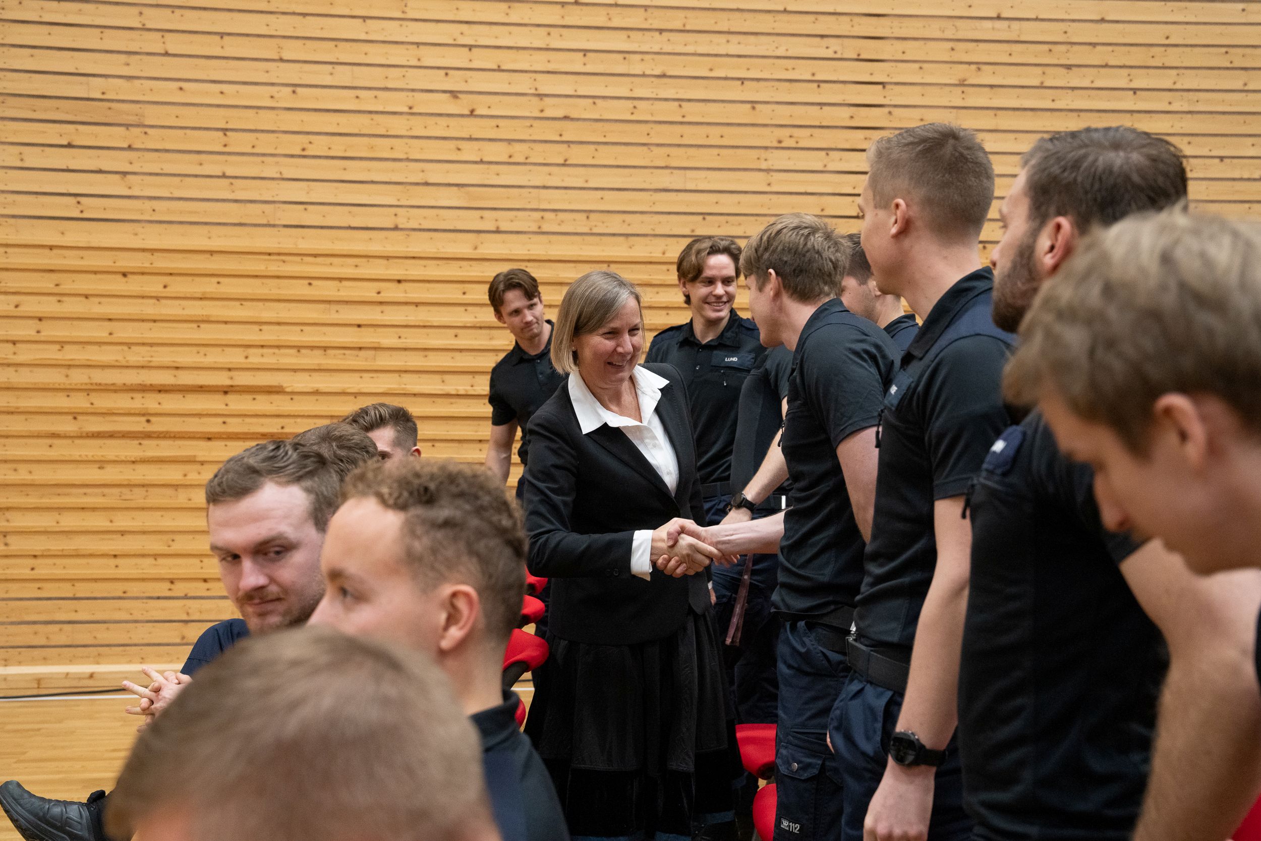 En dame i dress tar hånden til mannlige uniformerte studenter