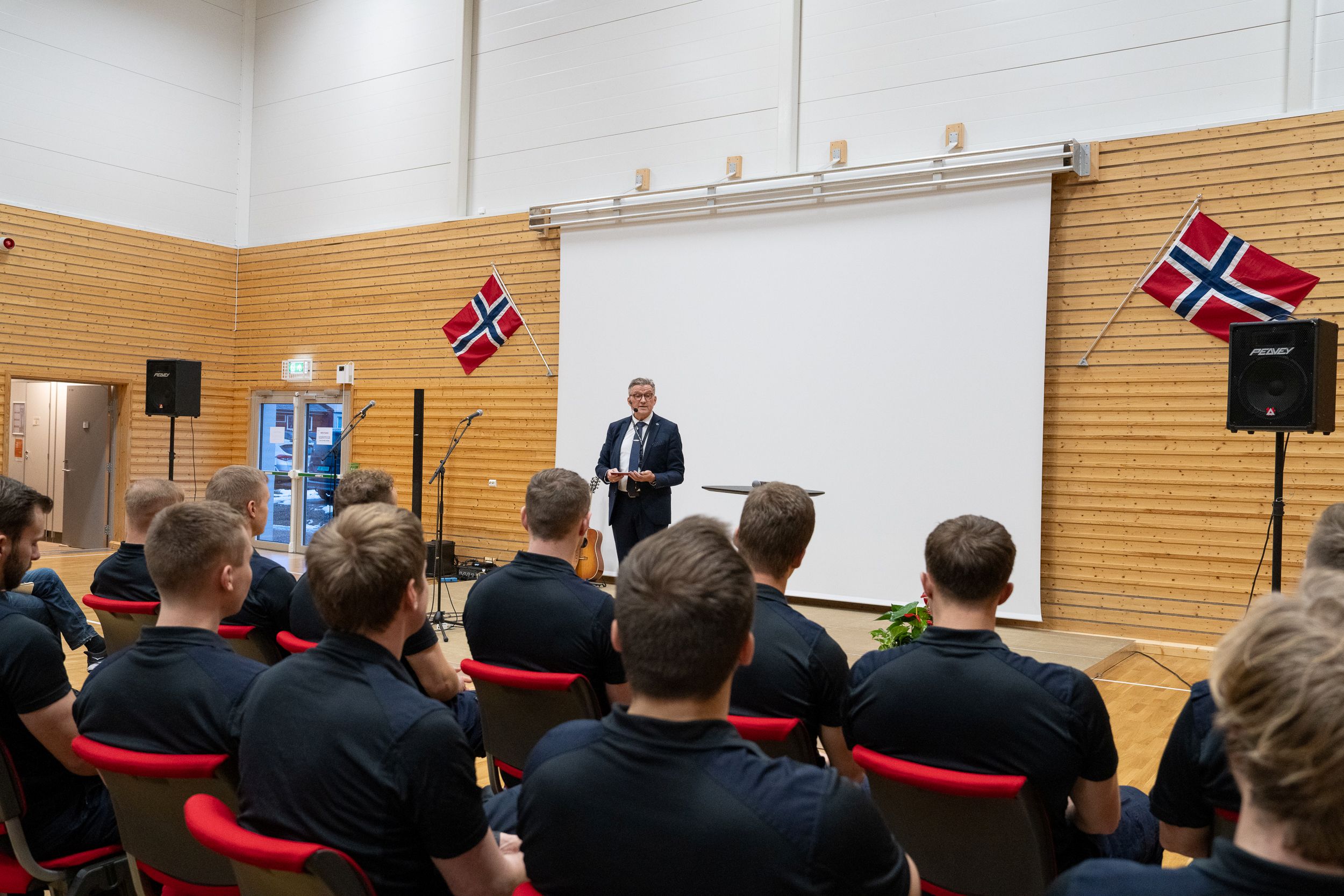 Mann i dress står foran et publikum og holder tale