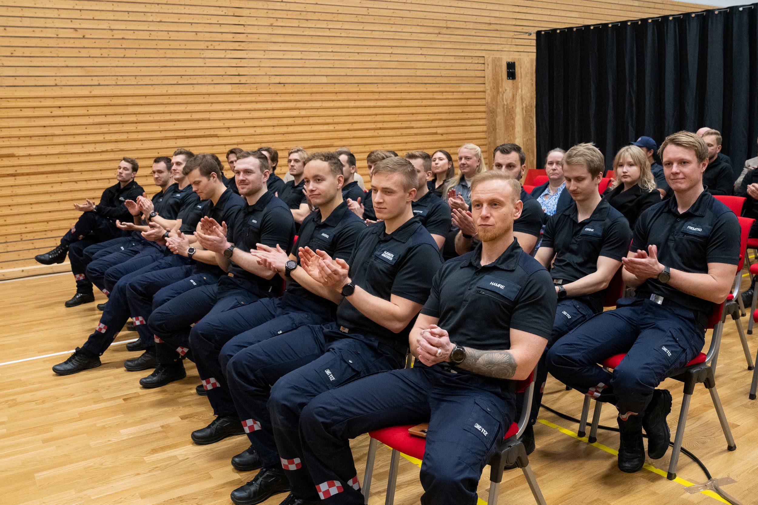 Mannlige studenter i uniform sitter på stoler i en gymsal