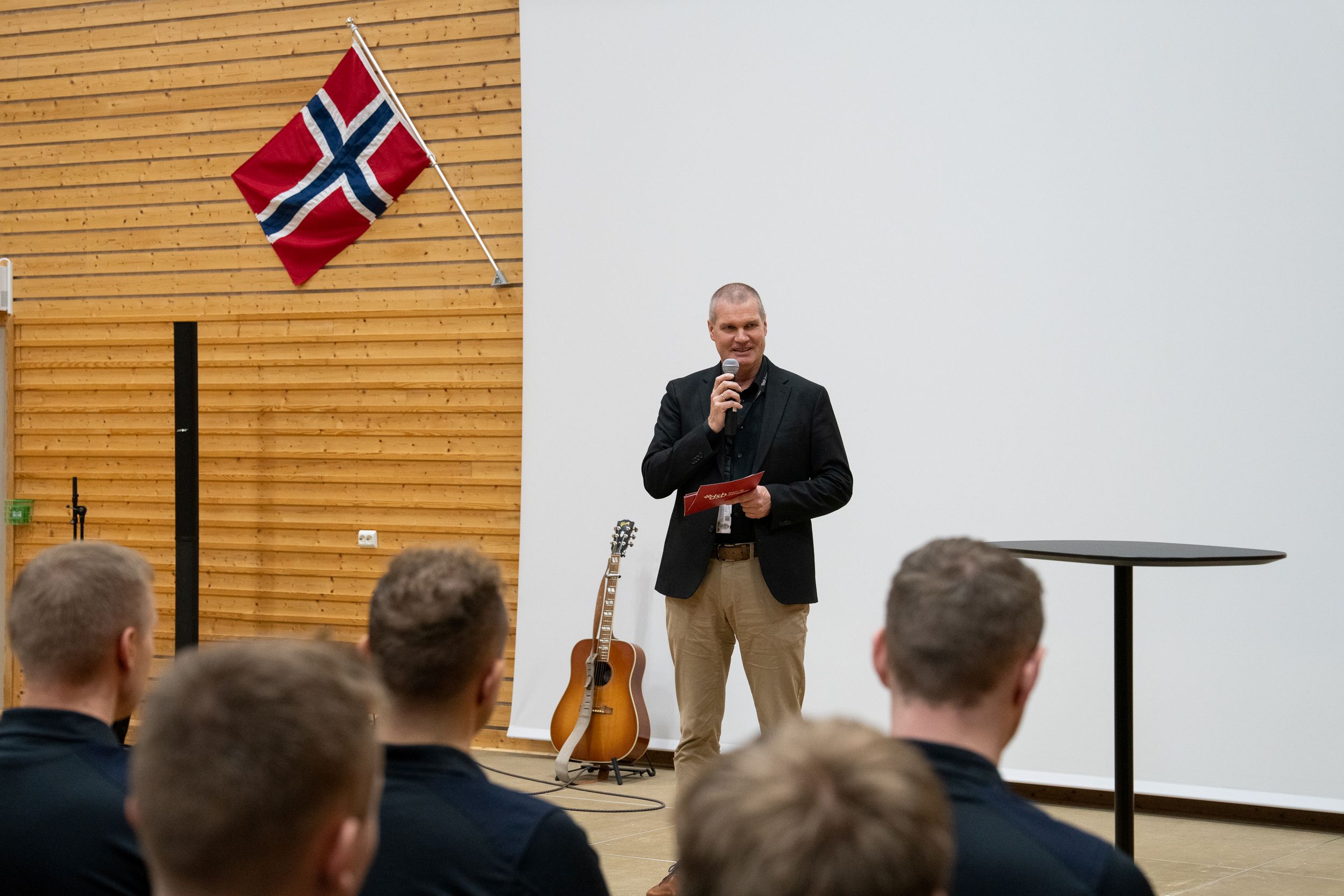 Mann står foran publikum og snakker. Det norske flagget på hans høyre side