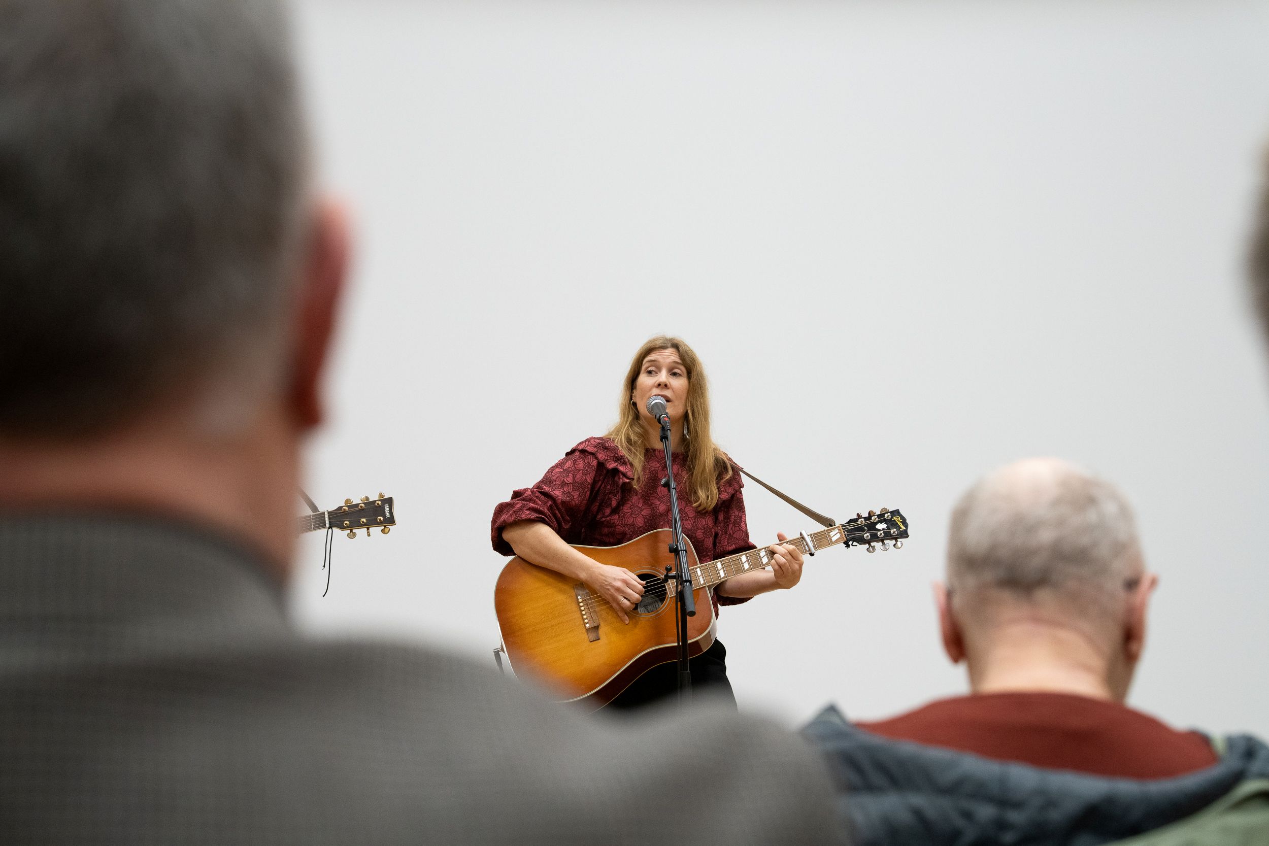 En dame står med gitar og synger i mikrofonen