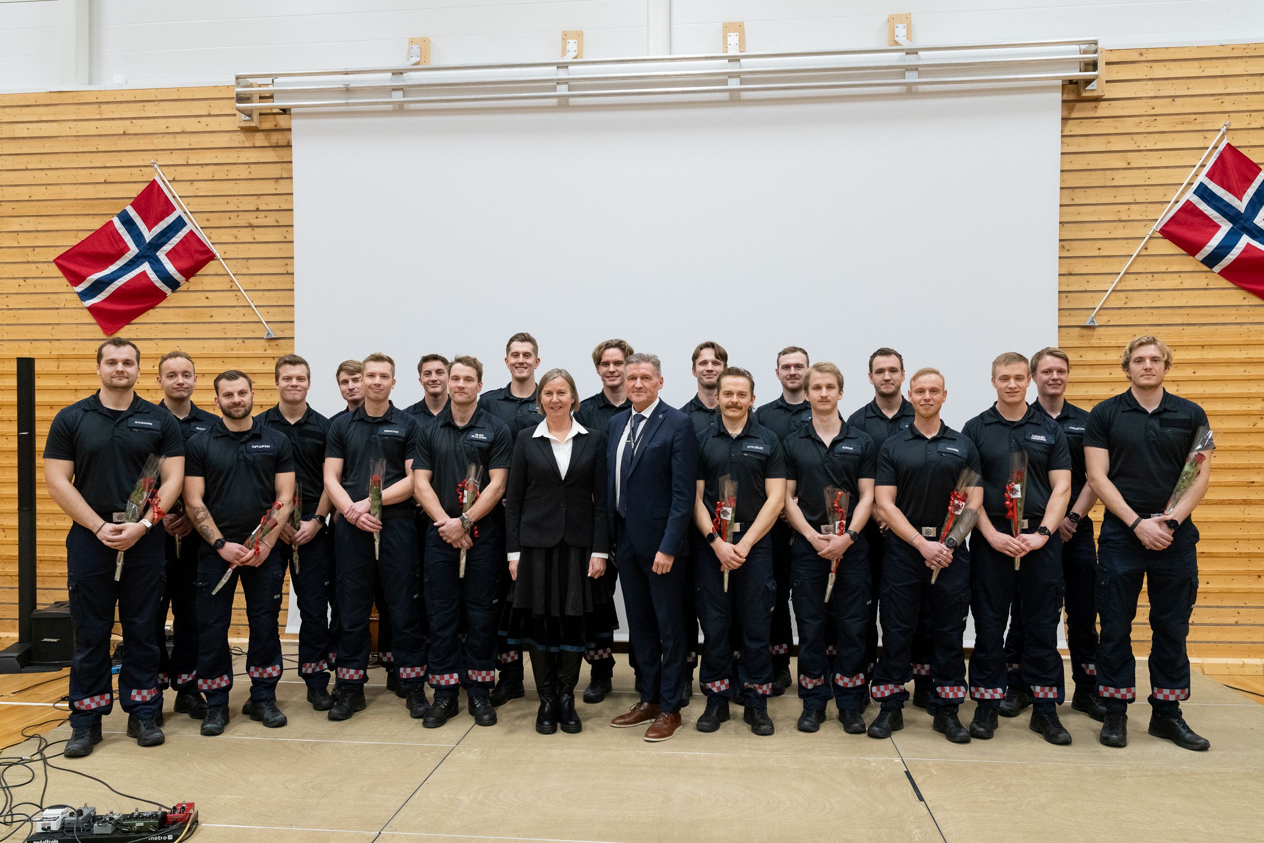 Gruppebilde av uniformerte studenter med en dresskledd kvinne og mann i midten.