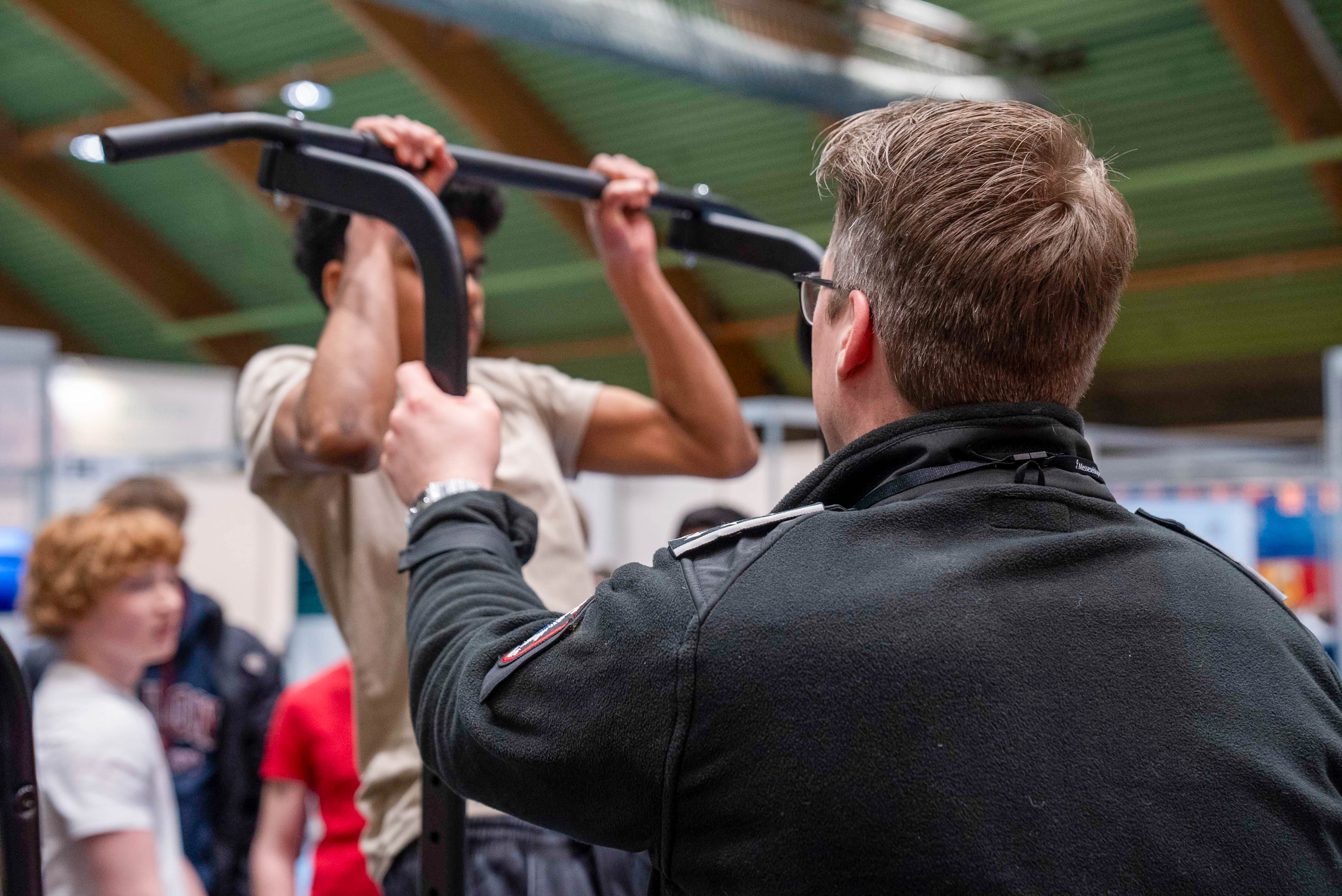 En elev henger fra et pullup stativ mens en ansatt observerer