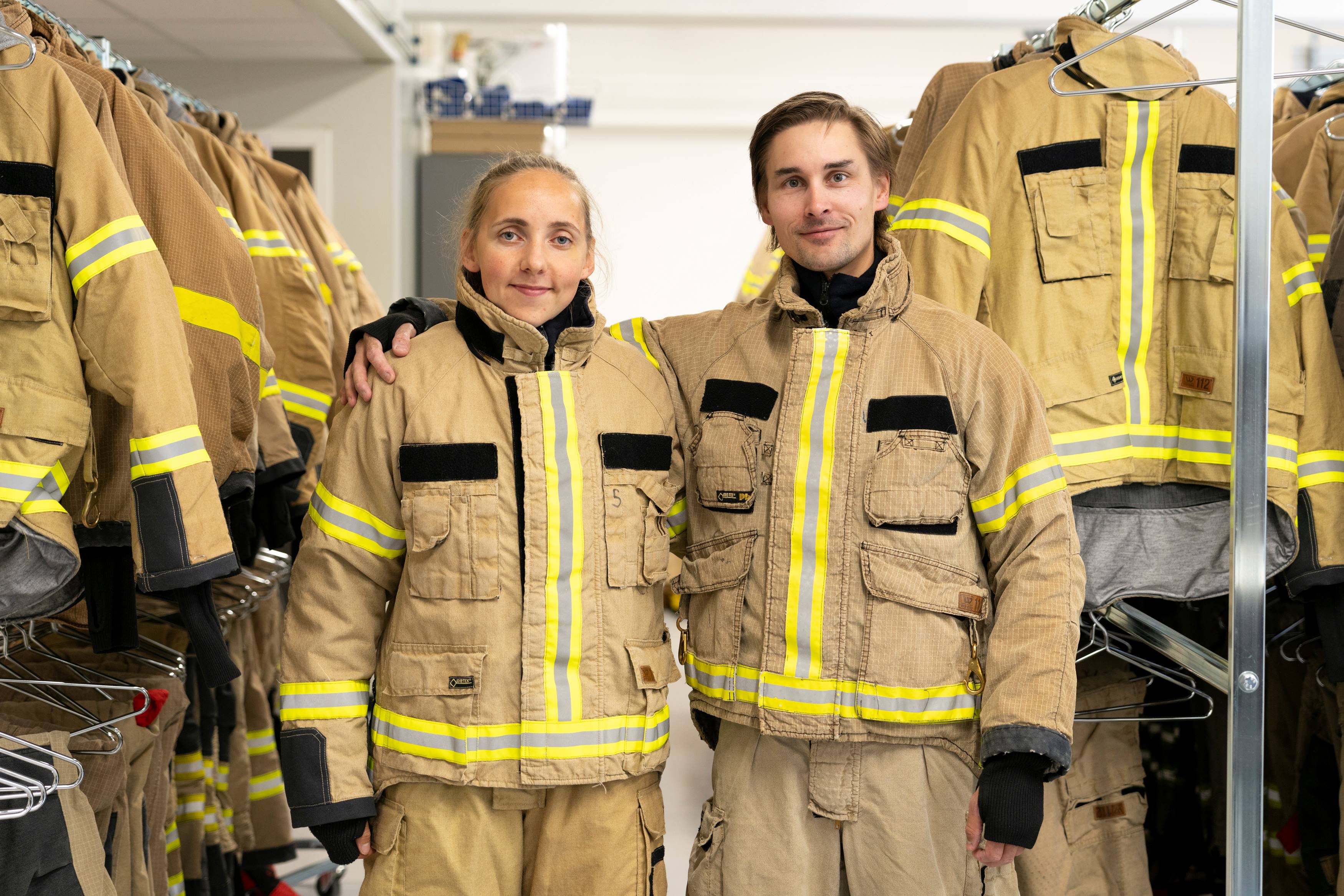 To studenter i brannbekledning holder rundt hverandre og smiler mot kamera