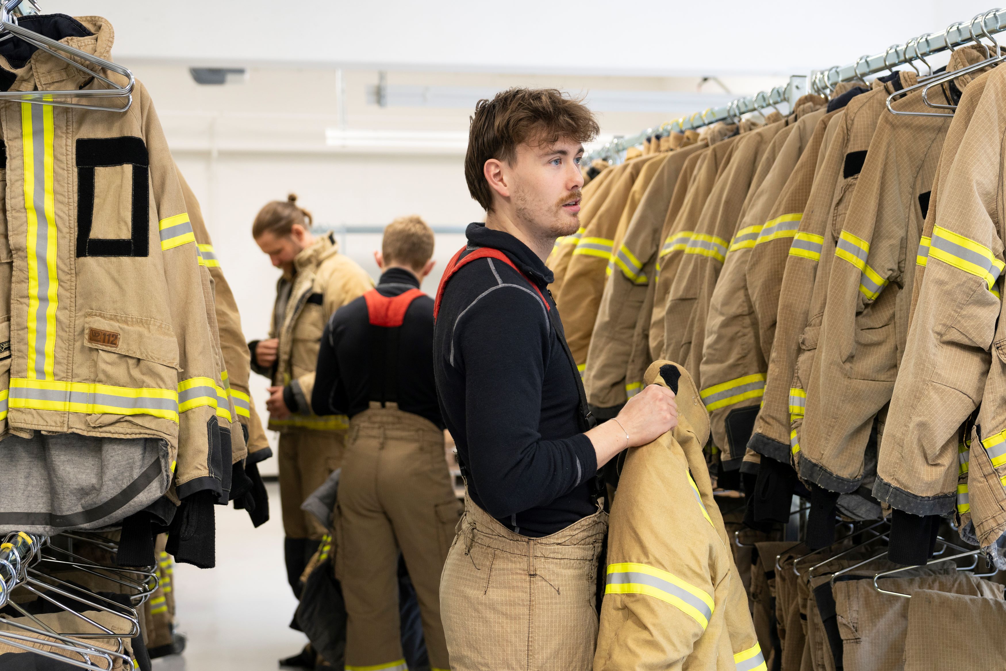 Tre studenter er i bekledningsrom med røykdykkerdrakter hengende på hver side 